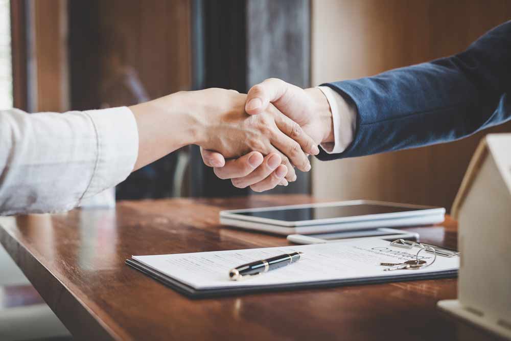 Handshake across a desk with documents and a tablet
