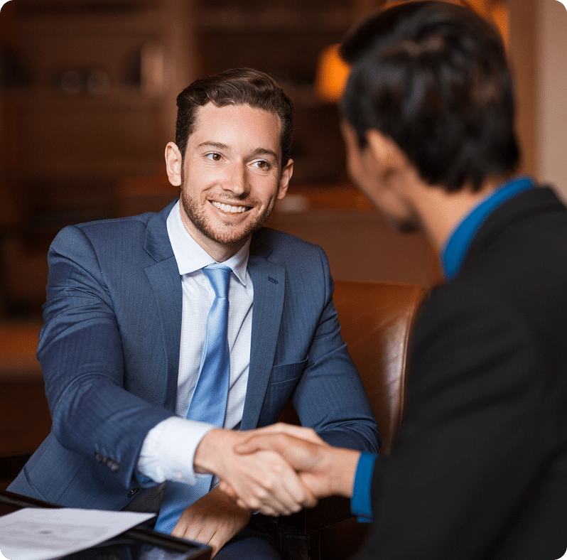 Two men in suits shaking hands across a table