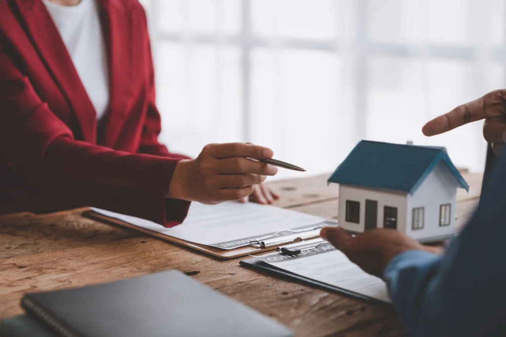 Two people discussing paperwork beside a model house