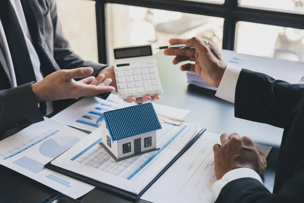People reviewing figures with a calculator beside a model house