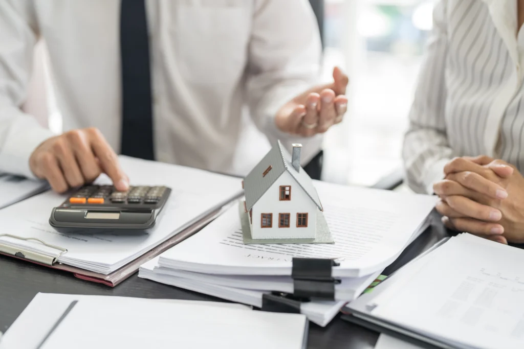 People at a desk with a calculator, paperwork and a model house