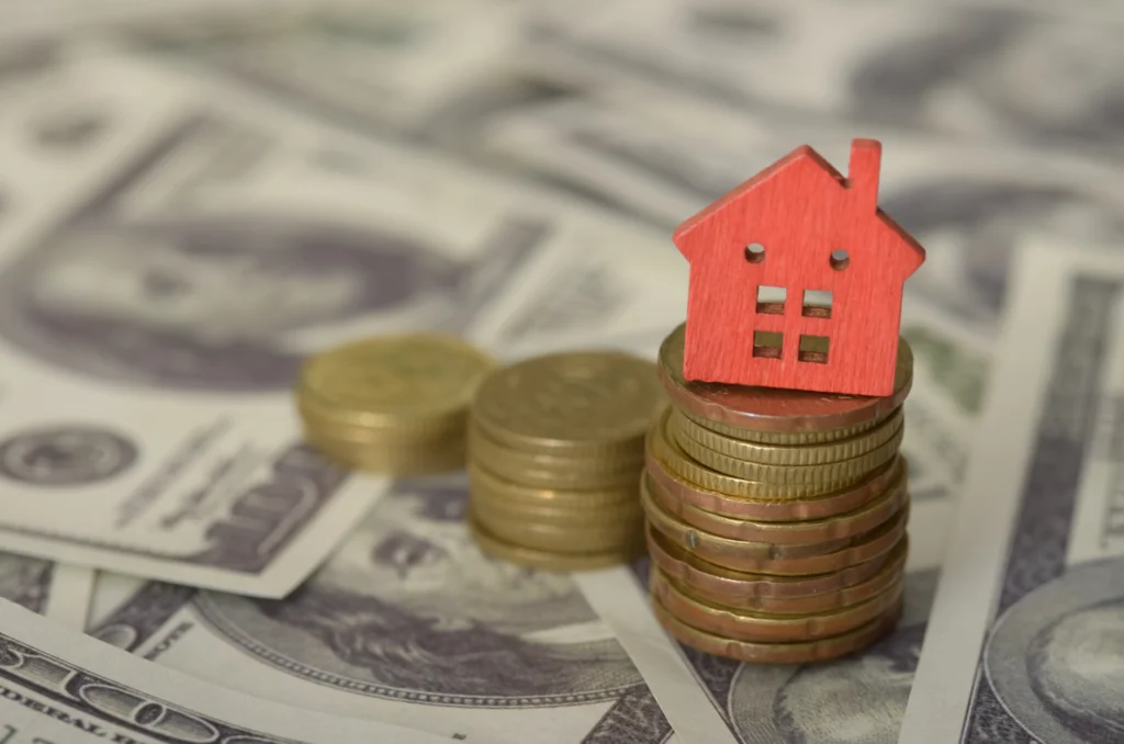 Red model house on a stack of coins over dollar bills