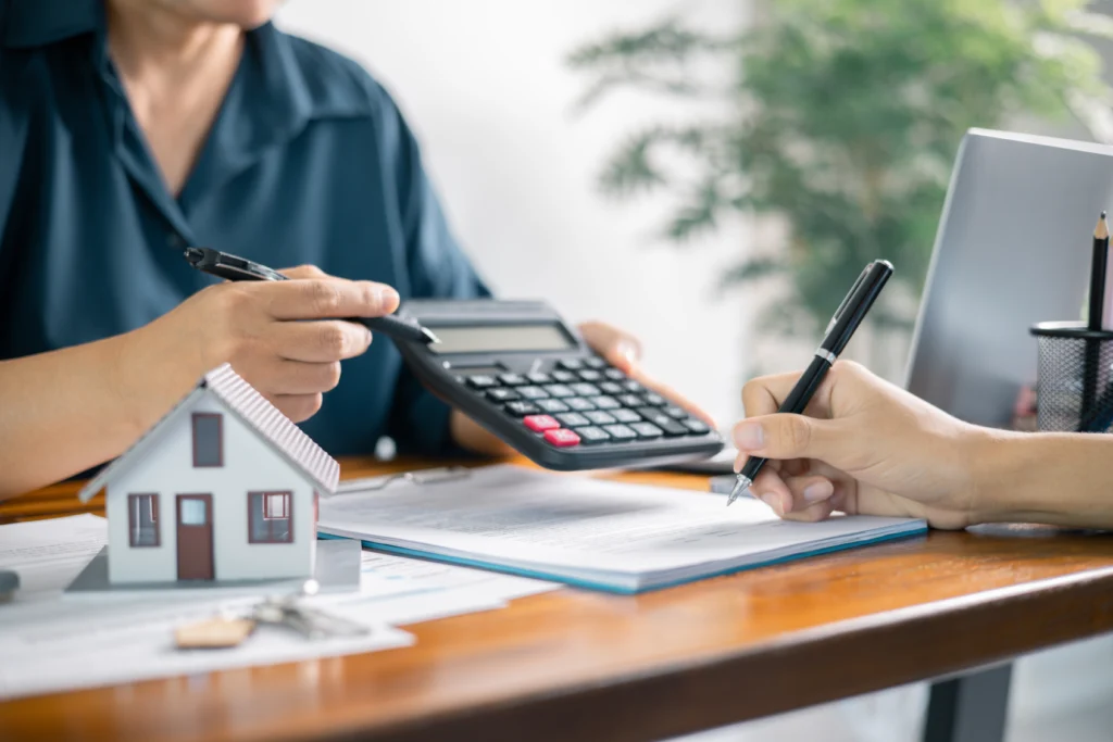 Two people working through paperwork with a calculator and a model house