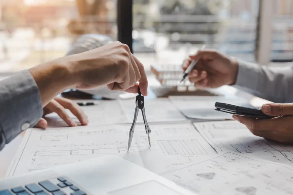 Hands working over architectural drawings with a compass