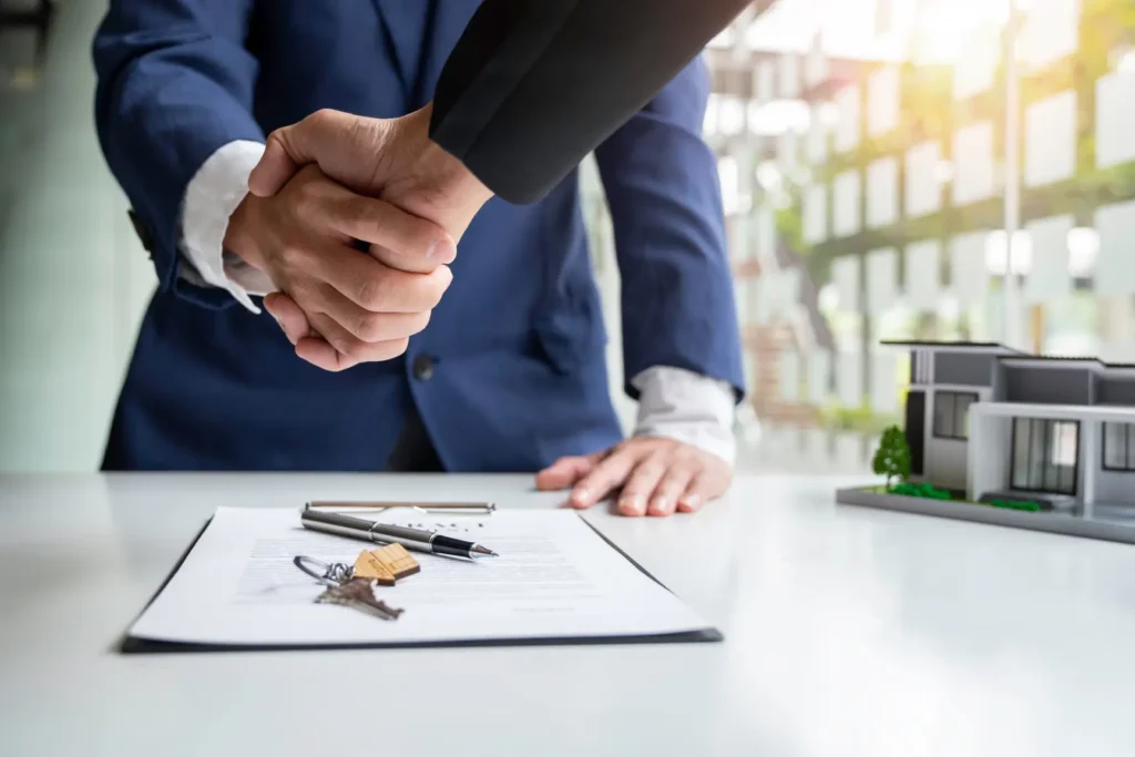 Handshake over a contract and keys beside a model building