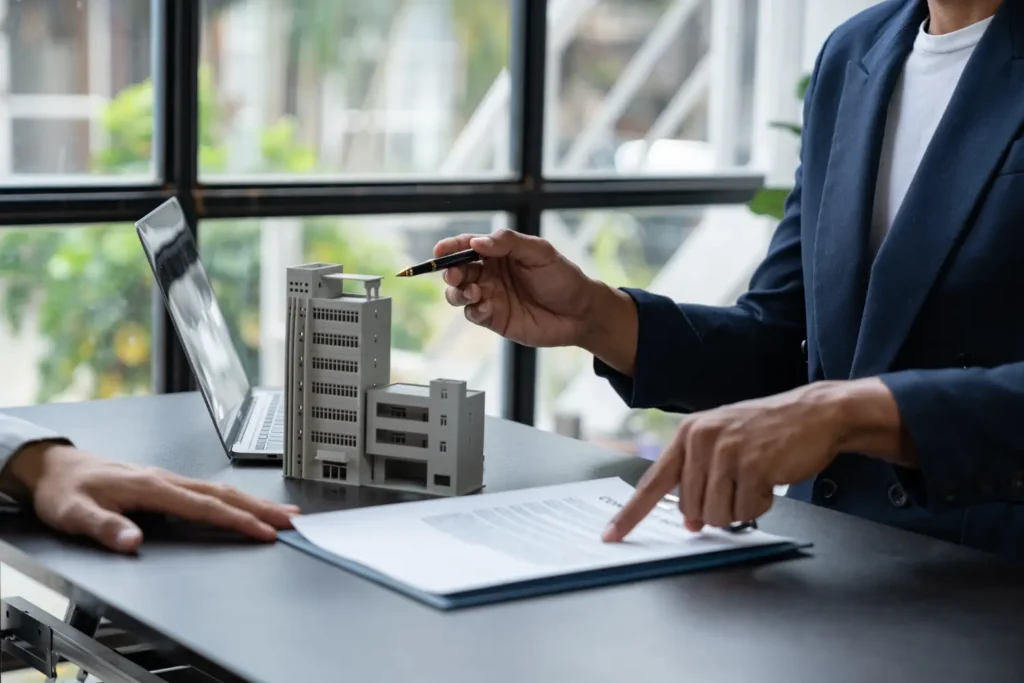 Person pointing at a document beside a model apartment building