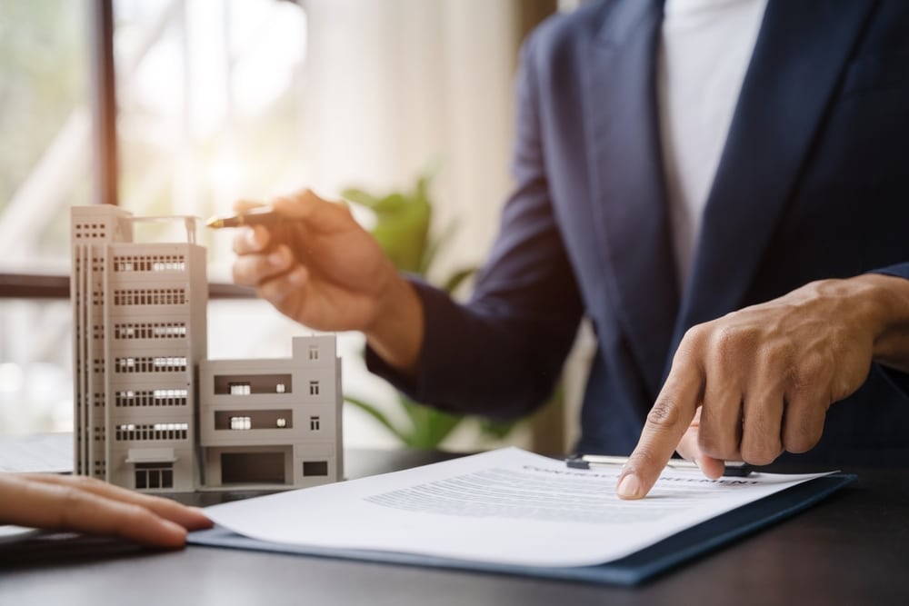 Person pointing at a contract beside a model apartment building