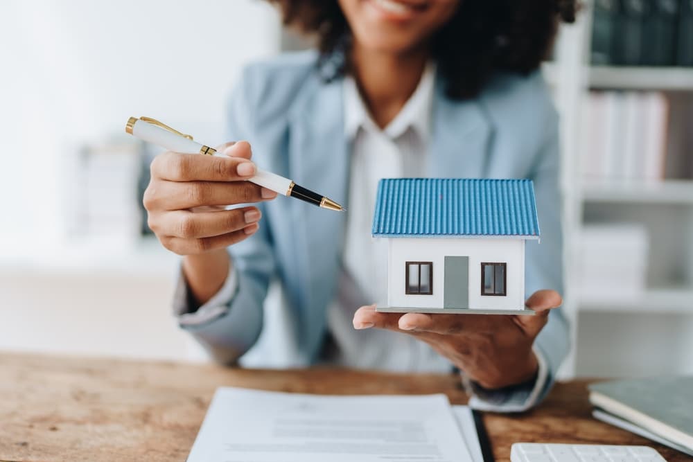 Woman holding a model house and pointing at it with a pen