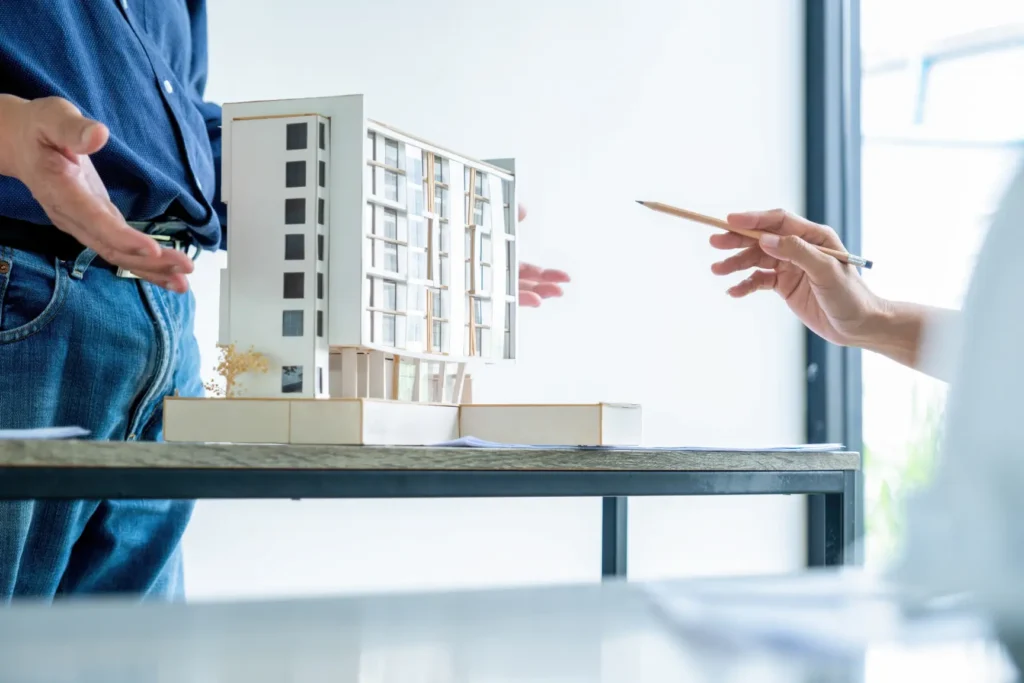 People discussing a model apartment building on a table