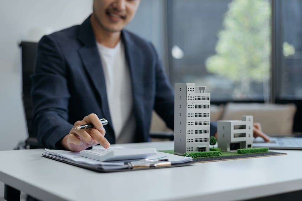Man in a blazer writing beside model apartment buildings