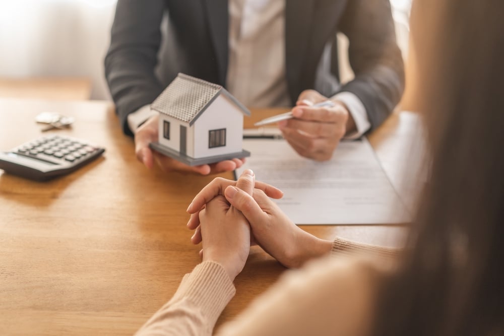 Two people at a desk with a model house and a calculator