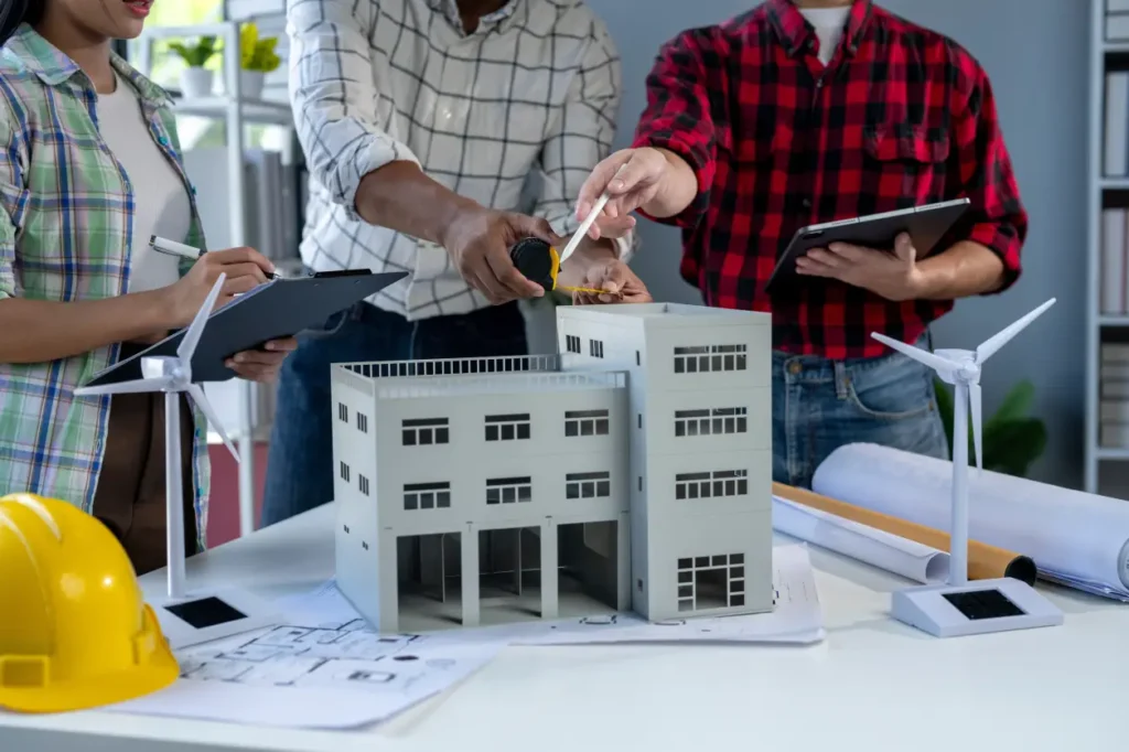 Team with tablets around a model building and a hard hat