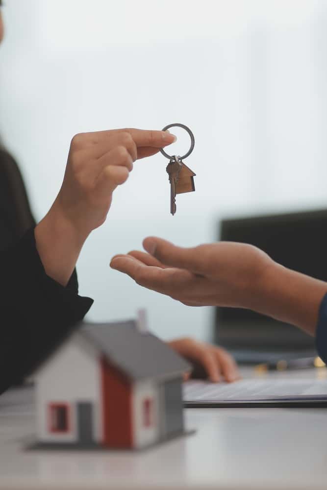 Hand passing a key over a red-roofed model house
