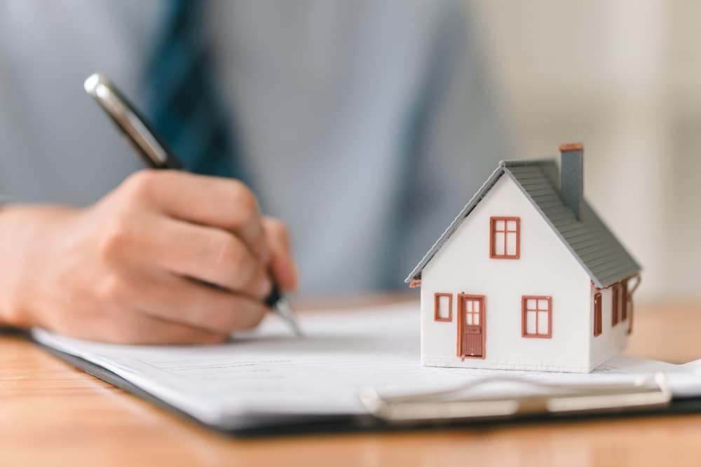 Hand signing a document beside a model house