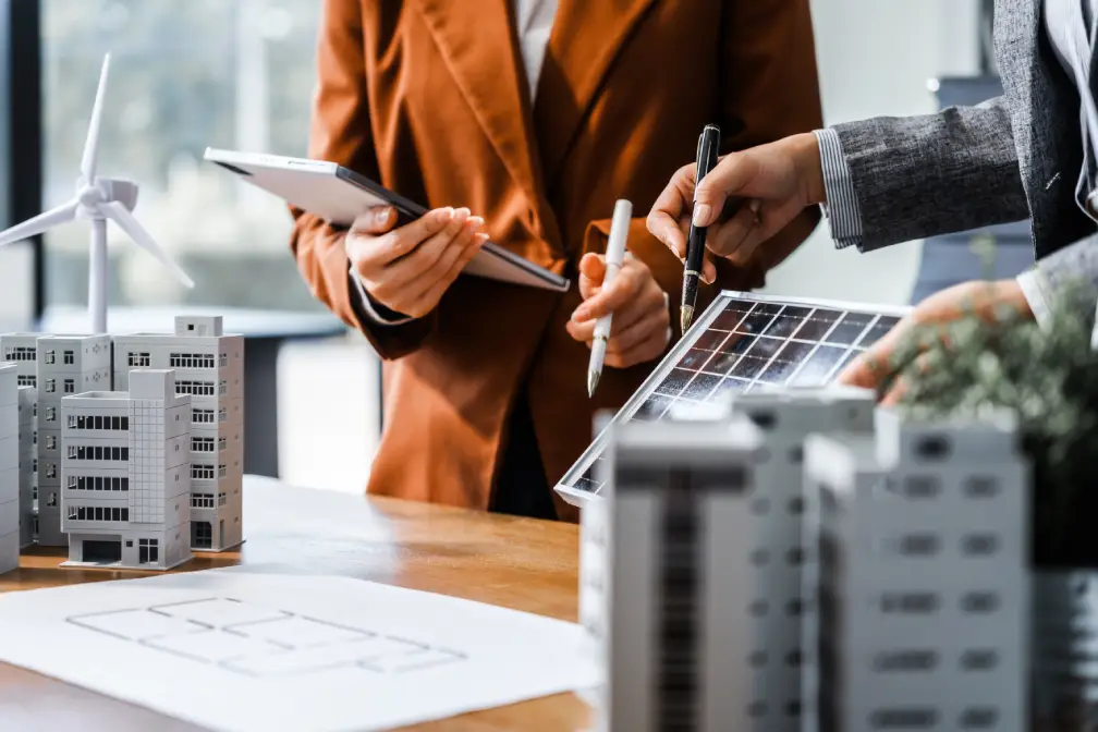 People reviewing plans beside model buildings and a wind turbine model
