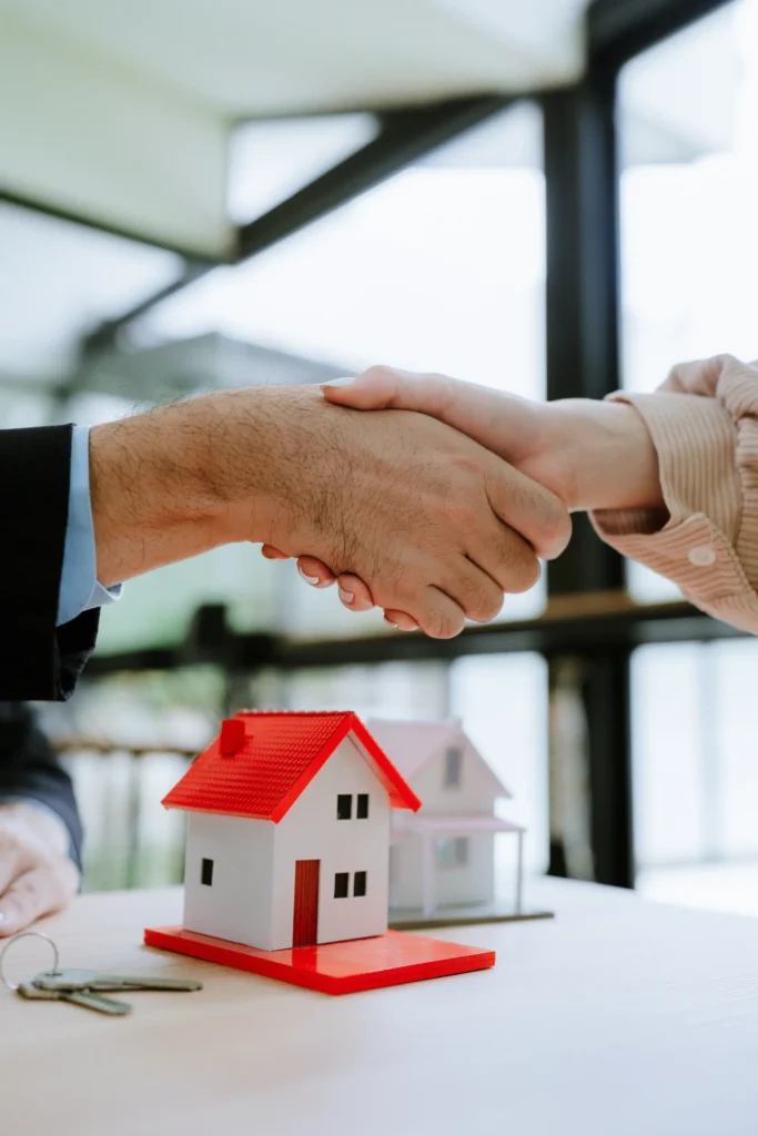 Handshake above a red-roofed model house