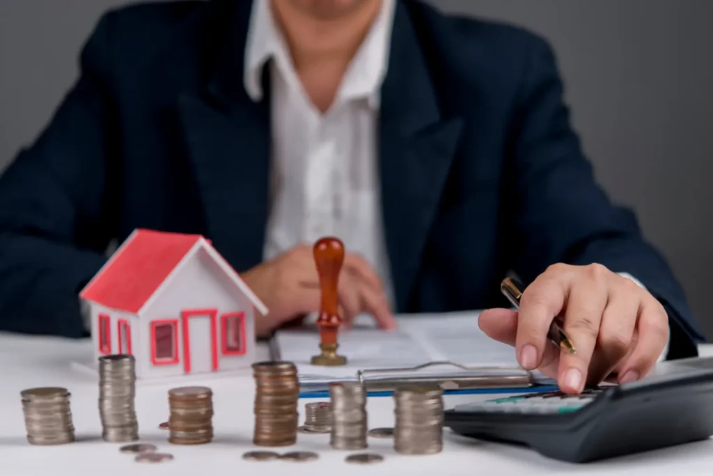 Person with a model house, stacked coins and a rubber stamp