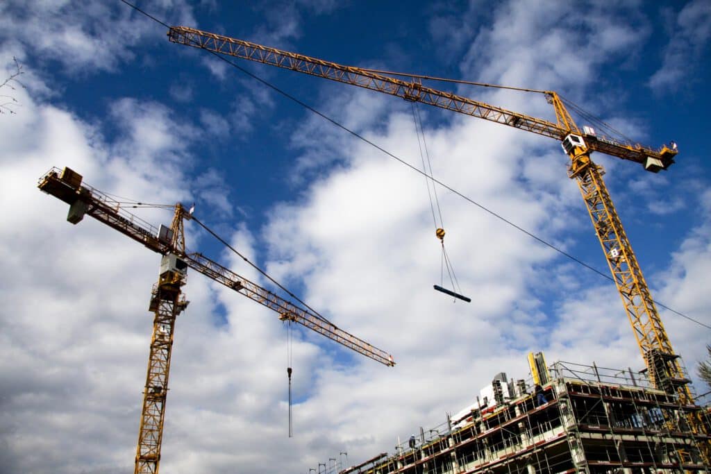 Two tower cranes against a cloudy sky